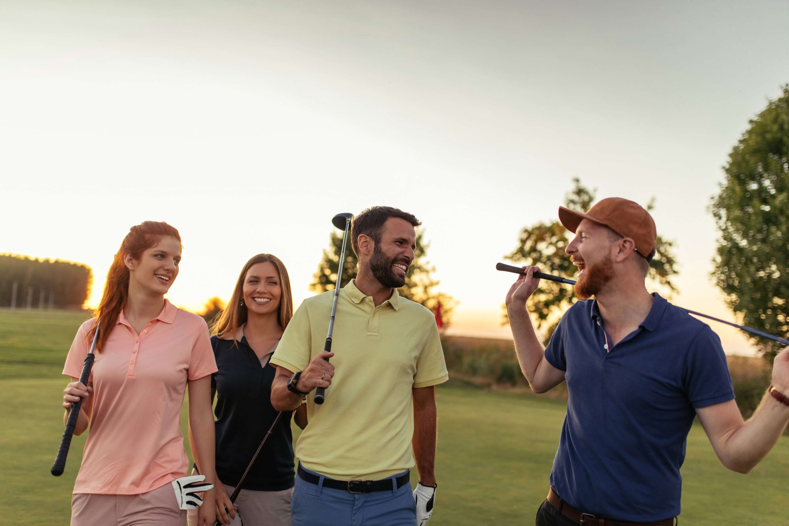Group of happy golfers walking the golf course at sunset | Featured image for the Golf and Wellness – Exploring the Mental & Physical Benefits of Golf blog from Brookwater Residential.