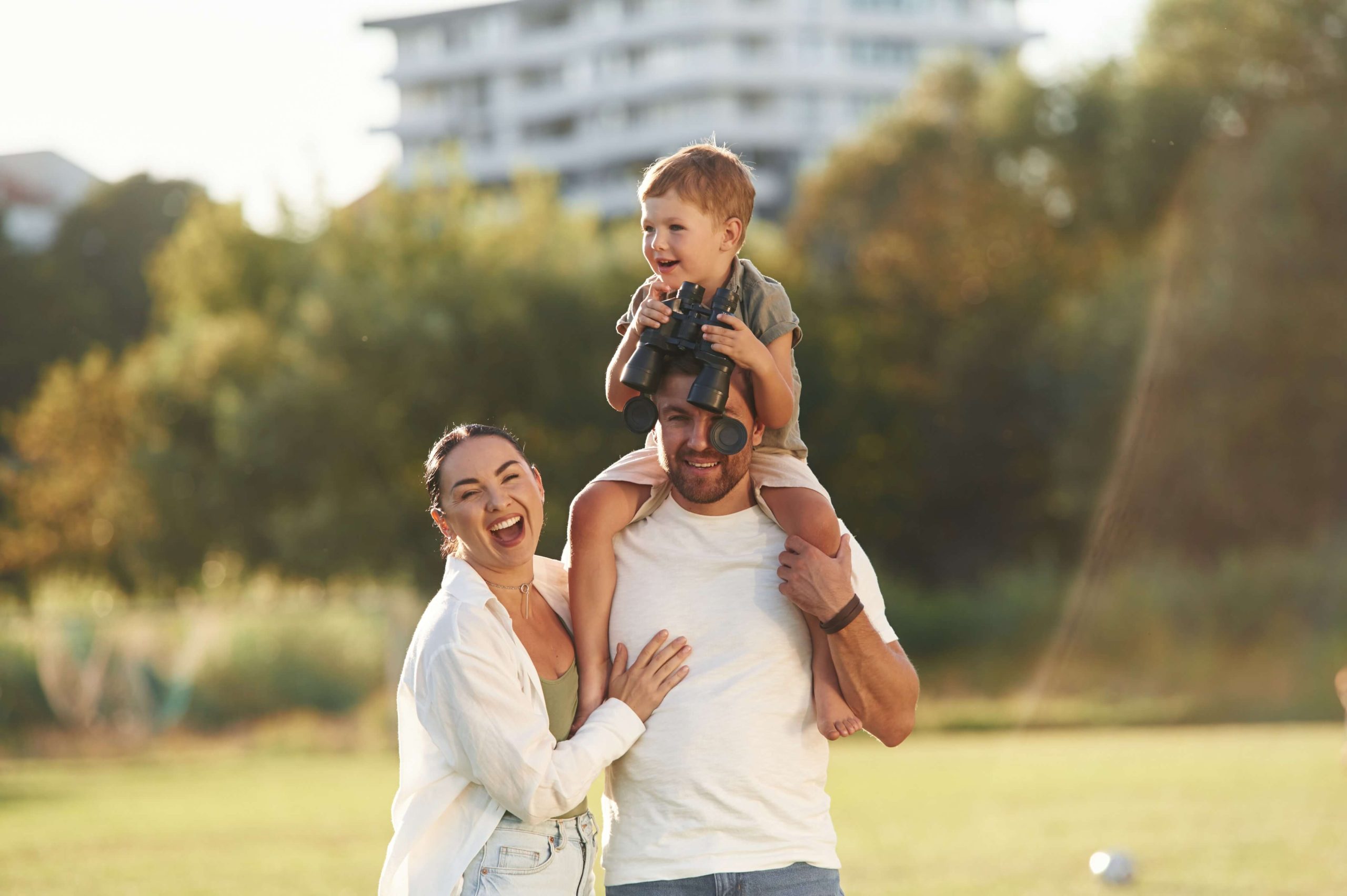 Mother and father with their son outdoors on the field laughing | Featured image for the Modern Urban Living – What Buyers Are Looking for in 2025 blog from Brookwater Residential.
